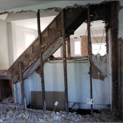 Load-bearing wall opened up with temporary posts and stairs exposed during structural demolition