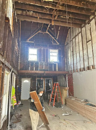 Worker carrying lumber out of a tall barn interior stripped back to original framing