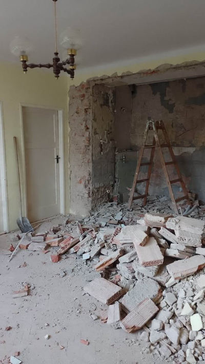 Large masonry opening cut through an interior wall with brick and plaster rubble on the floor