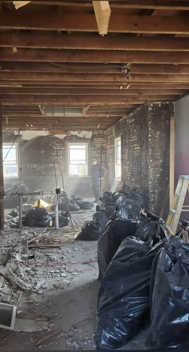 Crew member sweeping a fully gutted interior with exposed brick walls and bagged demolition debris