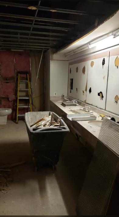 Commercial washroom mid strip-out with fixtures removed and debris cart on site