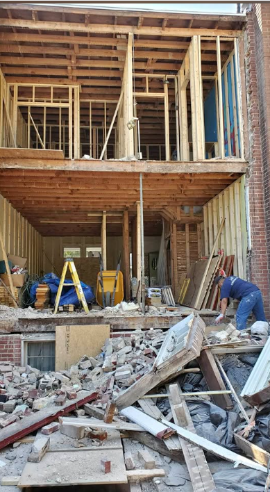 Two-storey rear wall removed exposing framed floors while a worker sorts salvaged material