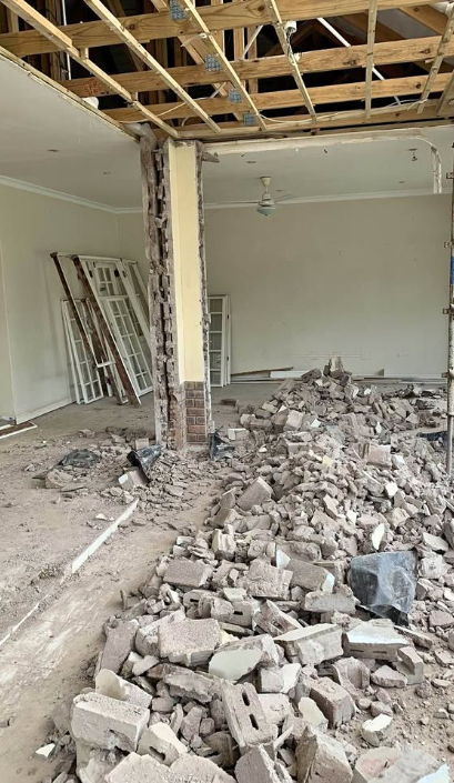 Interior brick wall demolished with rubble piled on the floor and ceiling stripped to joists