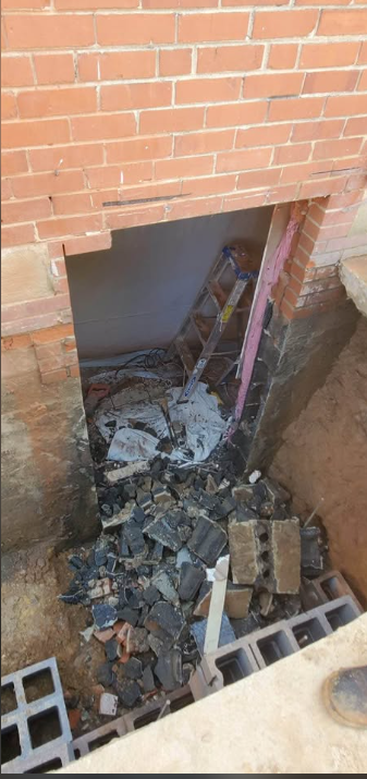 New foundation opening cut through brick with broken concrete block stacked outside
