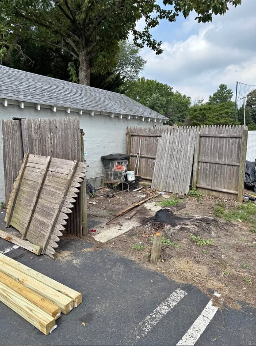 Wood fence panels dismantled and stacked in a paved yard with a stump ground out