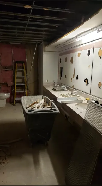 Commercial washroom mid strip-out with a debris cart and fixtures removed