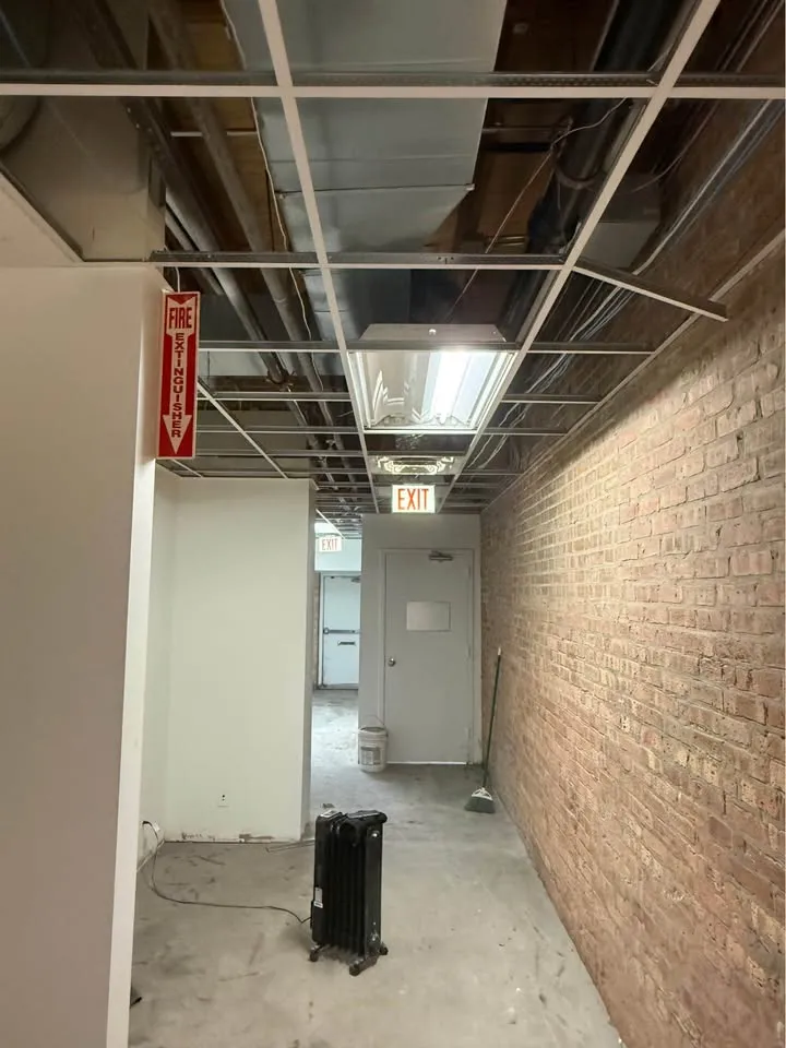 Commercial corridor with the ceiling grid exposed and the floor cleared