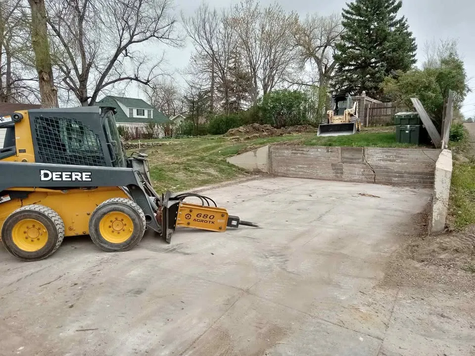 Skid steer with a hydraulic breaker working on a residential driveway