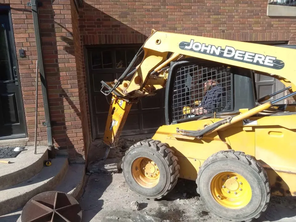 Skid steer working at the front steps of a brick house