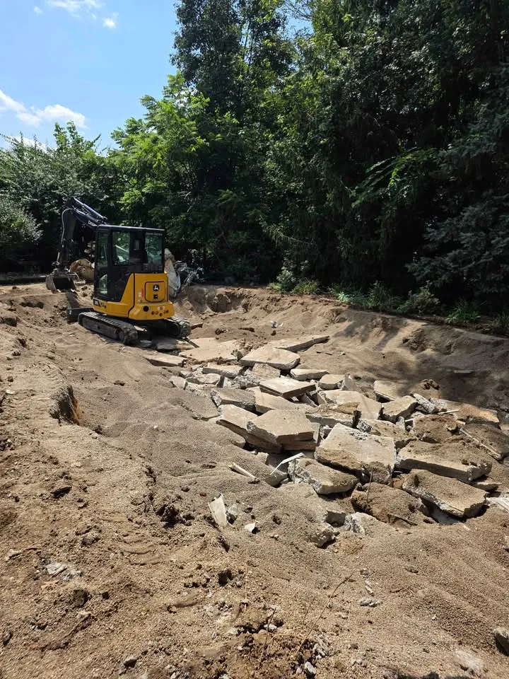 Mini excavator stacking broken concrete slabs in a backyard