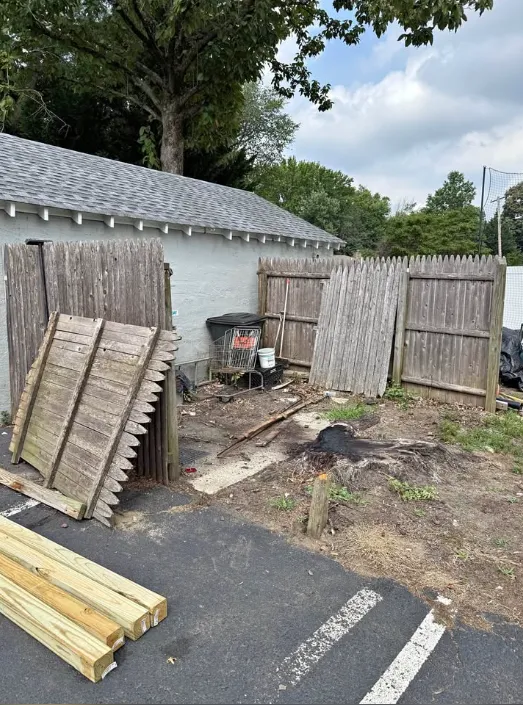 Wood fence panels dismantled and stacked beside a paved yard