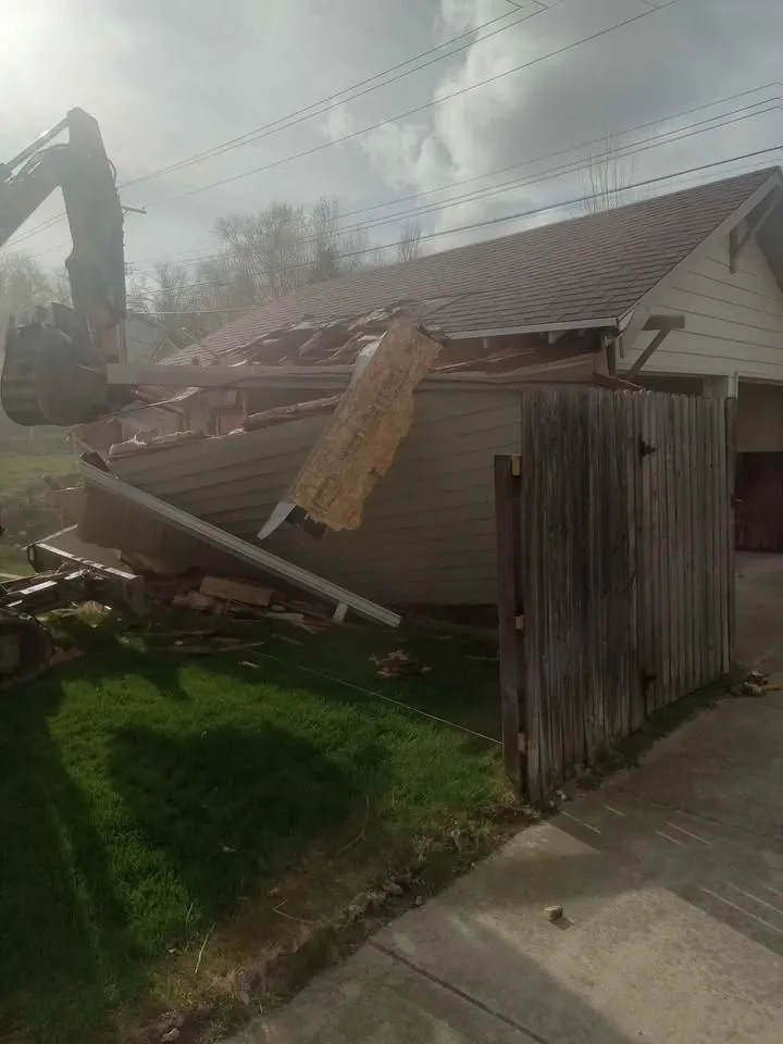 Excavator taking down a detached garage right beside a neighbour's wood fence