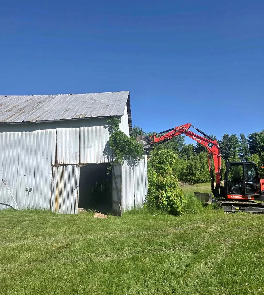 Compact excavator starting on a metal-clad barn on a grass lot