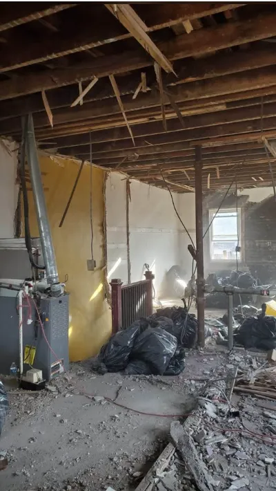 Main floor opened to the ceiling joists with furnace in place and bagged debris along the wall
