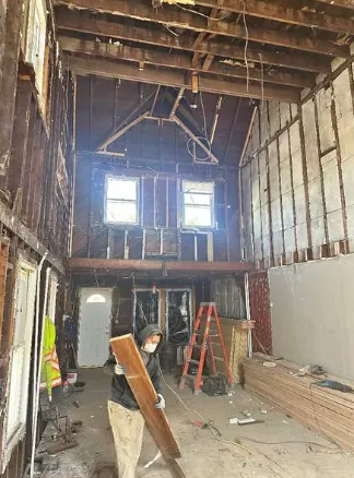 Crew member carrying lumber through a two-storey interior stripped to framing