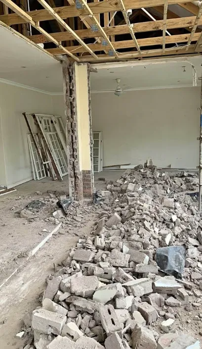 Masonry wall knocked through with brick rubble piled under an open ceiling