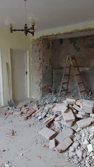 Brick and plaster wall opened up beside a ladder with rubble on the floor