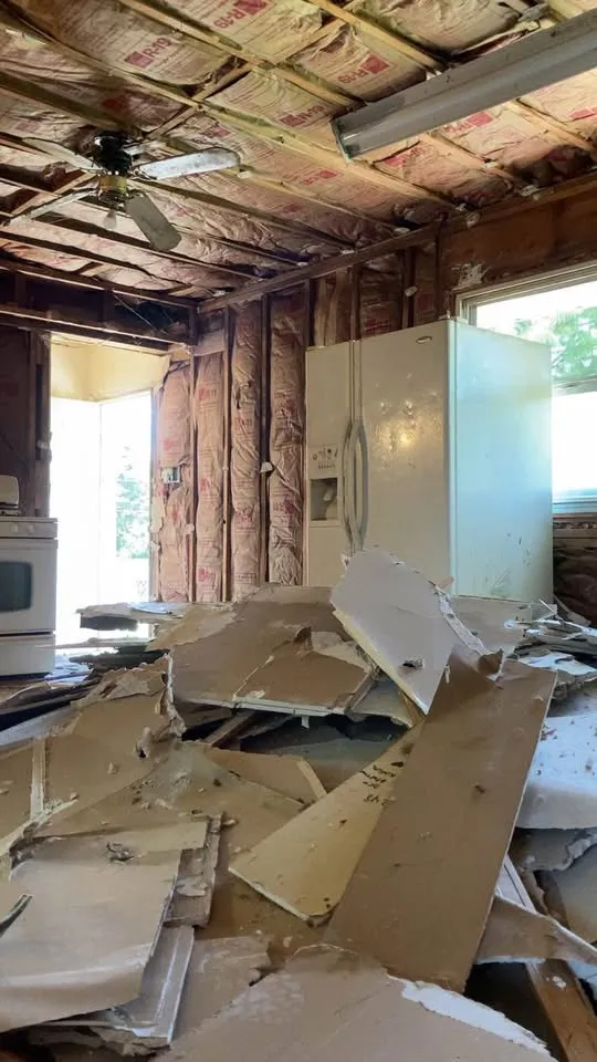 Kitchen ceiling opened with drywall debris heaped against the fridge