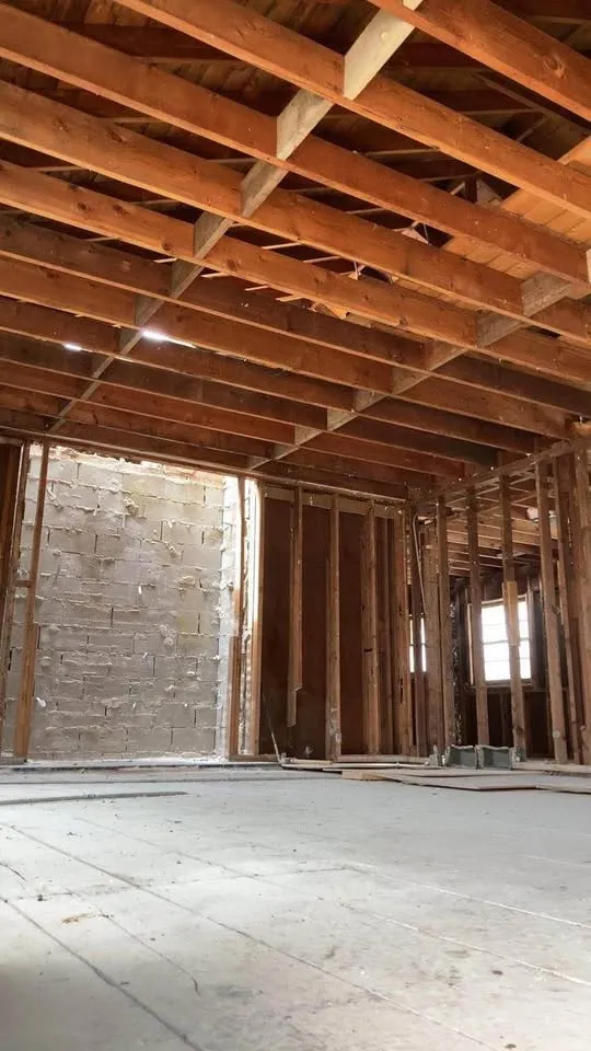 Room cleared to the joists and subfloor with a stone chimney wall behind