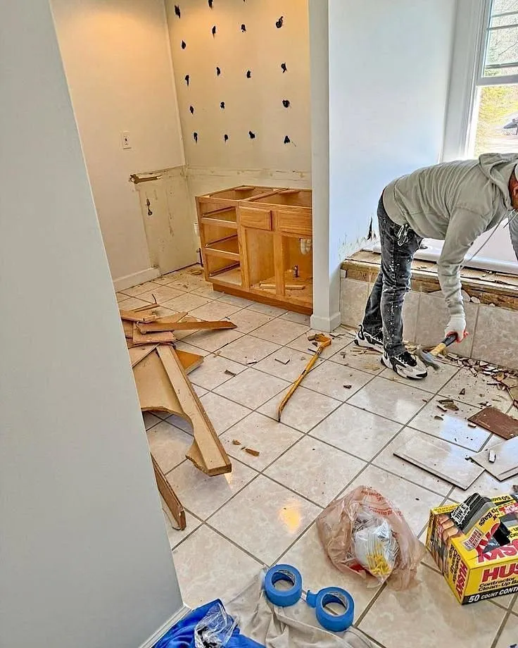 Worker prying up flooring in a bathroom after the vanity was removed