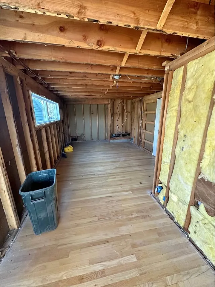 Upper room stripped to rafters with insulation exposed and hardwood swept clean