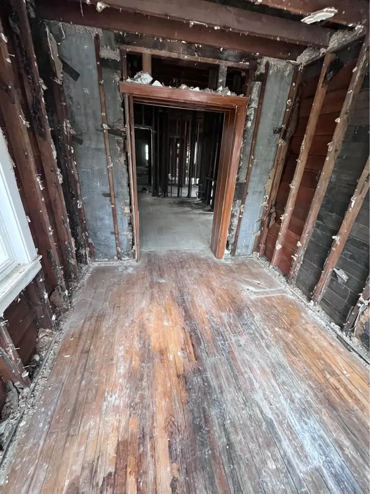 Hallway taken back to studs and door frames with worn hardwood underfoot