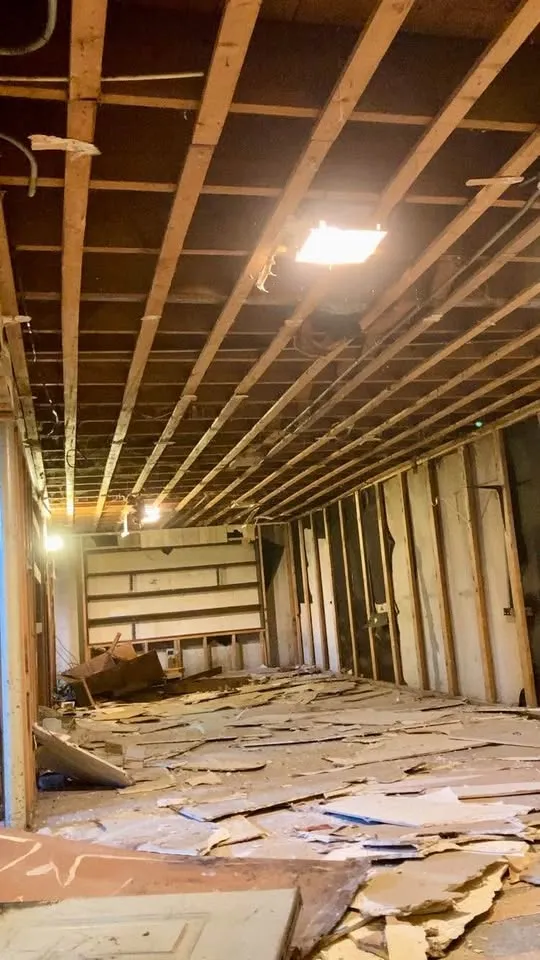 Long room stripped to ceiling joists and wall studs with drywall across the floor