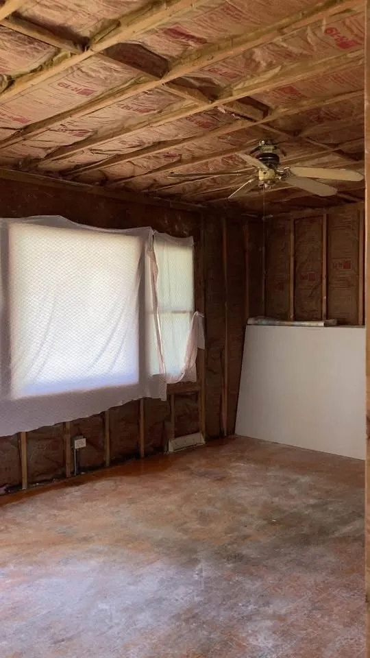 Bedroom with ceiling drywall removed to the insulation and window covered in plastic