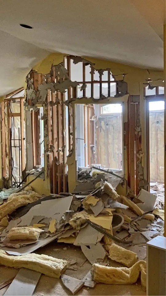 Partition walls knocked down to studs with batts and drywall piled on the floor