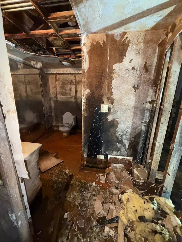 Damaged basement bathroom with debris and insulation on the floor after walls came down