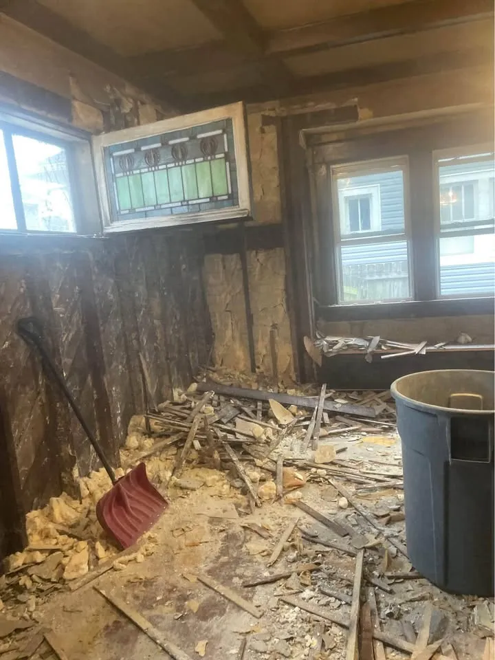 Room in an older home with plaster pulled back beneath a stained-glass window