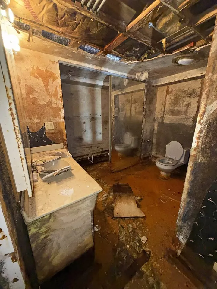 Damaged basement bathroom with vanity and toilet still in place and ceiling opened