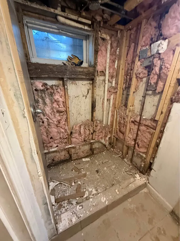 Shower stall stripped to studs and pink insulation with tile removed from the base