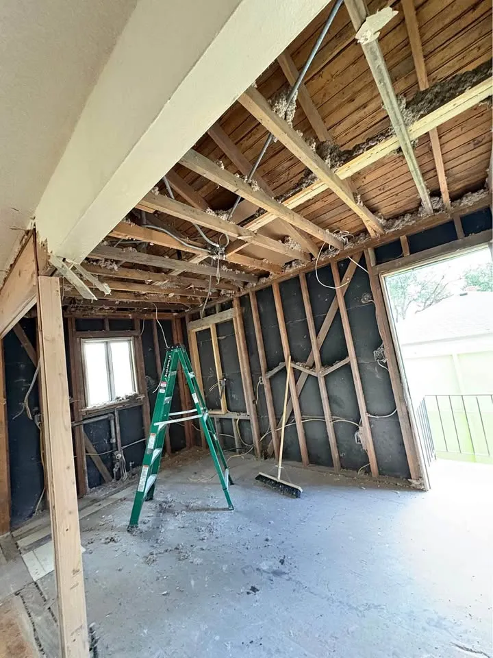 Room stripped to studs and ceiling joists with a ladder and broom on the swept floor