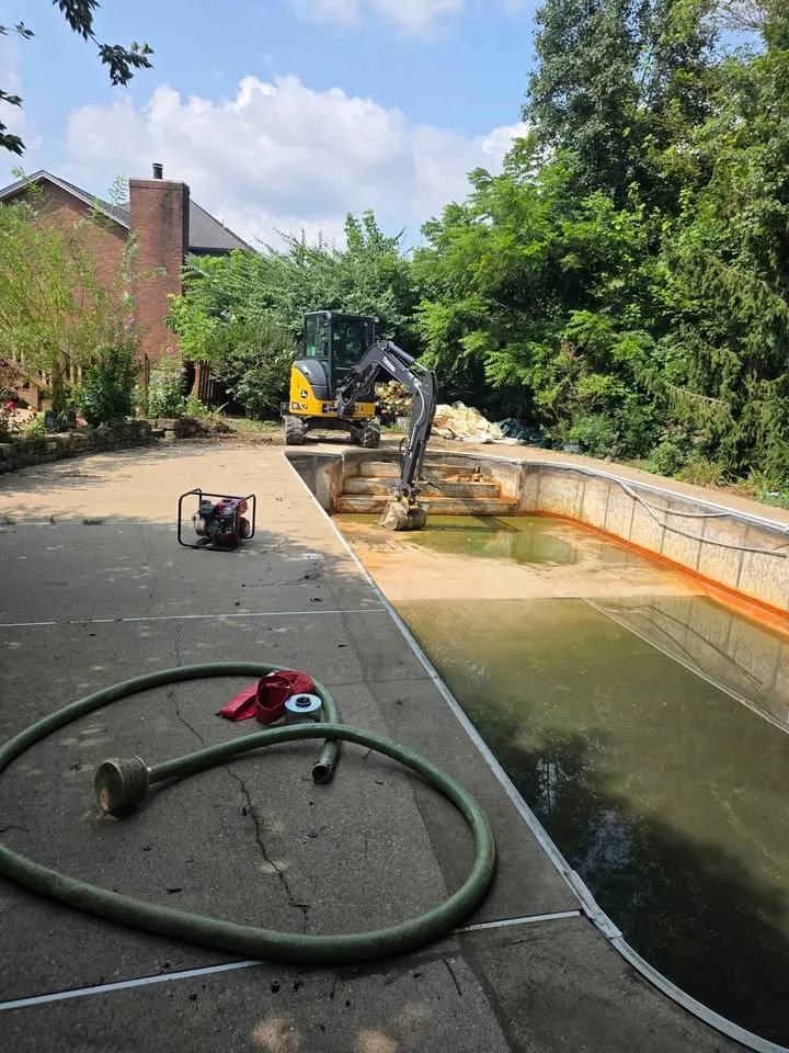 Mini excavator in the shallow end of an inground pool while a pump drains the water